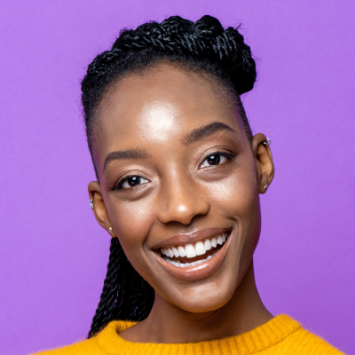 Portrait of a smiling woman with braided hair, wearing a yellow sweater against a purple background.