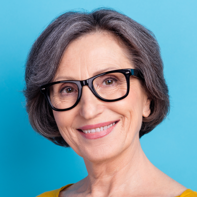 Elderly woman with gray hair and black glasses smiling against a blue background.