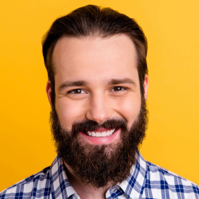 Portrait of a smiling bearded man in a plaid shirt against a yellow background.