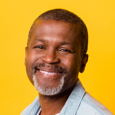 Middle-aged Black man with a goatee smiling warmly, wearing a light blue shirt against a bright yellow background.