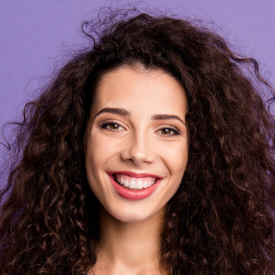 Portrait of a smiling young woman with curly hair against a purple background.