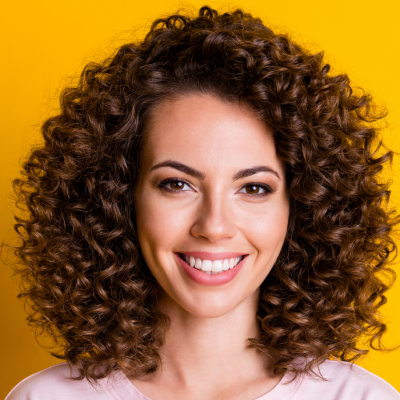 Portrait of a smiling woman with curly hair against a yellow background.