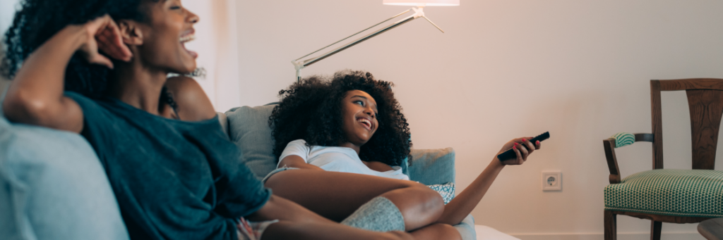 Two people relaxing on a couch, one holding a remote and smiling.