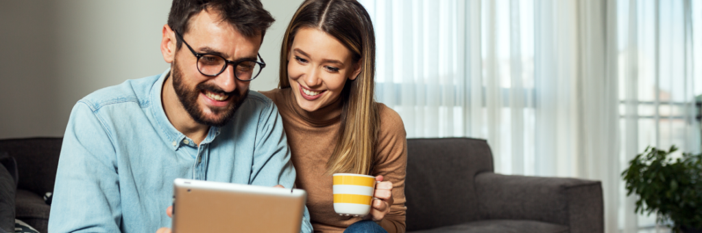 Two people smiling and looking at a tablet screen, one holding a coffee mug.