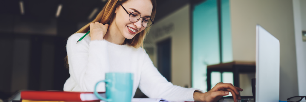 A woman smiling and working at a computer in an office environment.